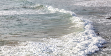 The ocean is calm and the waves are small. The water is a light blue color. The sky is clear and the sun is shiningの写真素材