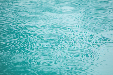 A body of water with raindrops falling on it. The water is a deep blue color, and the raindrops are...