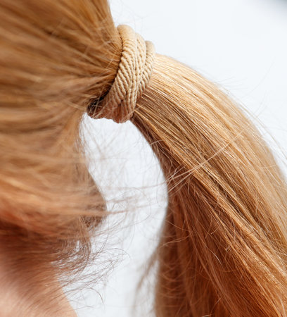 A girl with blonde hair has a ponytail. The ponytail is tied with a rope. The hair is long and is...