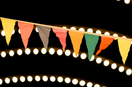 A string of flags hanging from a light fixture. The flags are of different colors and sizes. The lights are on and the flags are hanging from the ceilingの写真素材