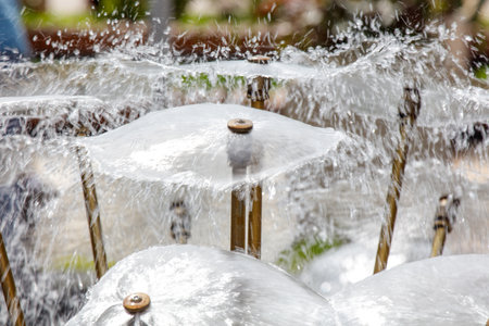 A group of umbrellas are spraying water in the air. The umbrellas are of different sizes and are arranged in a row. The scene is lively and playfulの写真素材