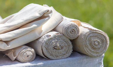 A stack of white fabric rolls are on a table. The rolls are all different sizes. The rolls are...