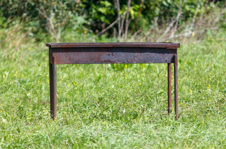 A metal grill stands on a grassy field. It is old and rusty. There are no people or animals in the frame.の写真素材