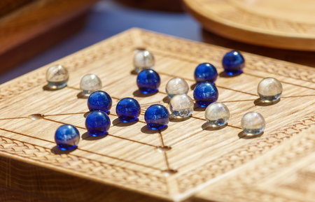 A wooden board with a pattern on it. There are many marbles on the board. Some are blue and some are whiteの写真素材