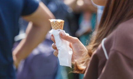 A woman holding a cone of ice cream with a napkin. She is wearing a brown jacket
