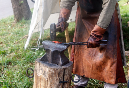 Man is forging a piece of metal with a hammer and an anvil. He is wearing leather gloves and an apronの写真素材