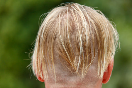 A boy with a shaved head. The hair is blonde and short. The boy is wearing a hatの写真素材