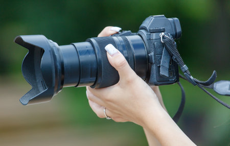 A person is holding a camera with a black lens. The lens is black and has a black strapの写真素材