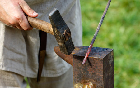 Man is hammering a piece of metal. He is using a stick to heat the metalの写真素材