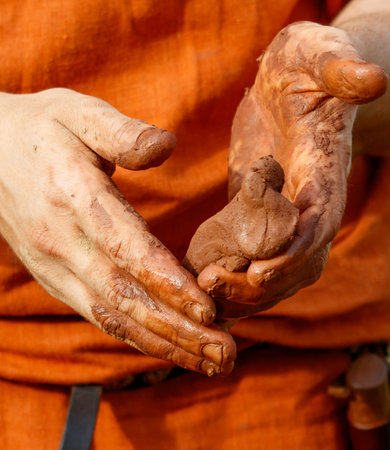 Man is holding a piece of clay in his hands. The clay is brown and has a rough textureの写真素材