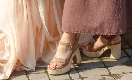 Two women wearing high heels. One is wearing a pink dress. The other is wearing a brown dress