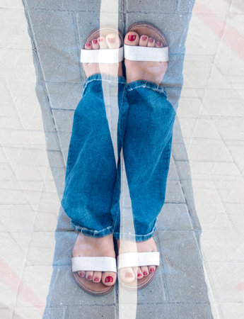 A woman wearing white sandals and red nail polish. She is standing on a brick sidewalk. The image is...