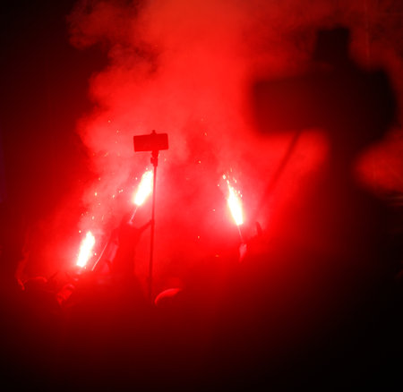 A group of people are standing in a red smoke filled area. One of the people is holding a cell phoneの写真素材