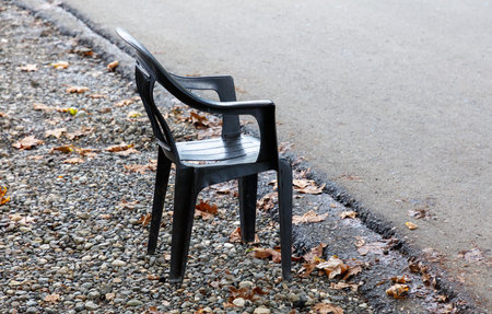 A black plastic chair is sitting on the side of a road. The chair is upside down and has a broken legの写真素材