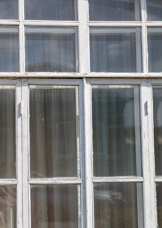 A window with white curtains and a white frame. The curtains are dirty and the frame is chipped