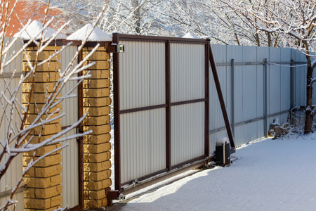 A gate is open and snow is on the ground. The gate is made of metal and is attached to a fence