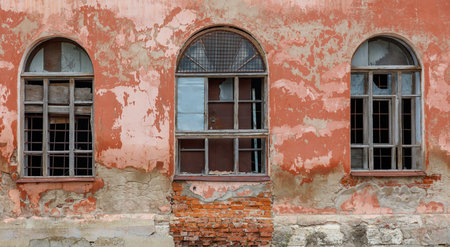 Three windows on a building with a brick wall. The windows are dirty and have broken glass. The...