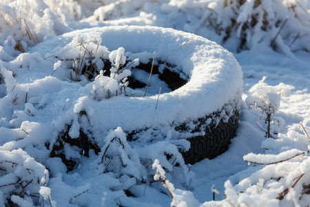 A tire is covered in a thick layer of snow, sitting on top of the snow-covered ground. The tire is...