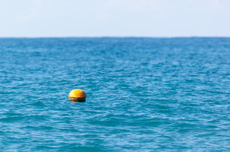 A yellow buoy is floating in the ocean. The water is blue and calm. The buoy is the only object in the waterの写真素材