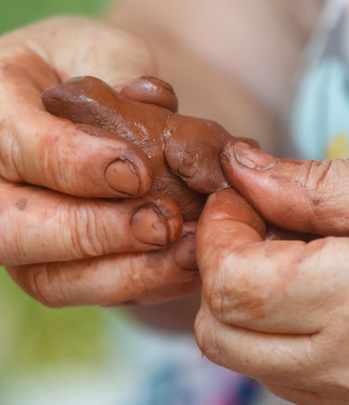 Person is holding a piece of clay in their hands. The clay is brown and has a rough textureの写真素材