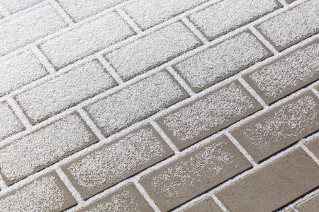 A brick wall covered in snow. The snow is white and covering the bricks. The bricks are gray and the...