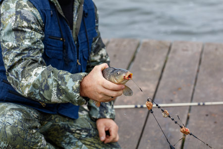 A man is holding a fish in his hand. The fish is biting the man's fishing lineの写真素材