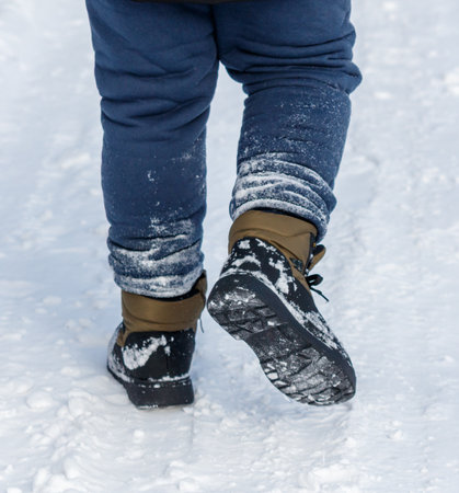 A person wearing blue pants and brown boots is walking in the snow. The boots are covered in snow and the pants are also covered in snowの写真素材