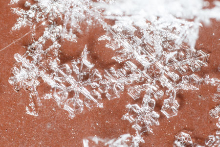 A snowflake is on a red surface. The snowflake is white and has a pointy tip