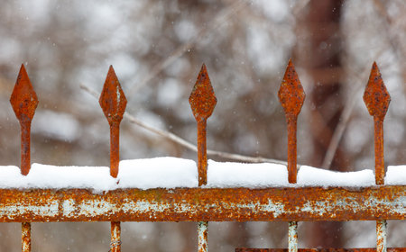 A rusty iron fence with snow on it. The fence has five spikes. The spikes are rusty and have snow on themの写真素材