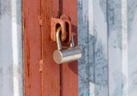 A rusty lock is hanging on a red door. The lock is silver and has a silver boltの写真素材