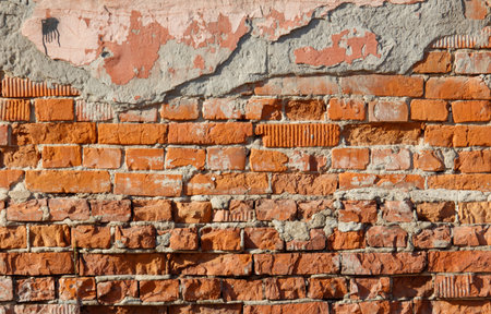 A brick wall with a few missing bricks. The wall is made of red bricks. The wall is old and has some cracksの写真素材