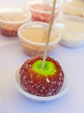 A green apple with a stick in it. The apple is in a white bowl. There are other bowls and containers in the backgroundの写真素材