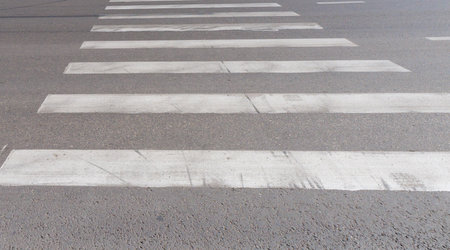 A crosswalk is painted on the road with white and black stripes. The stripes are evenly spaced and the white line is in the middle of the road. This is an important safety feature for driversの写真素材