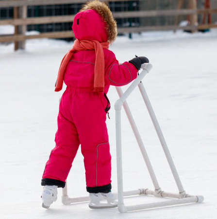 A child in a pink snowsuit is standing on a white plastic pipe. The child is wearing a red scarfの写真素材