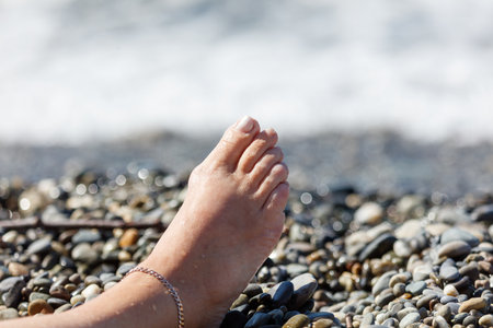 A woman's foot is laying on a beach. The sand is wet and the rocks are smallの写真素材