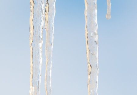 A long icicle hanging from a roof. The icicle is clear and has a blue sky in the backgroundの写真素材
