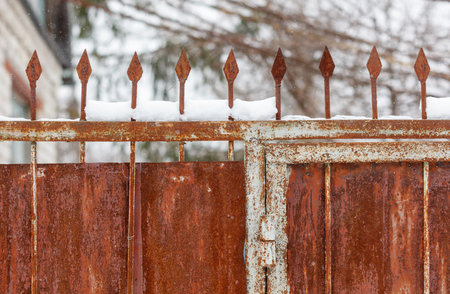 A rusty gate with spikes on it. The gate is covered in snow. The gate is on the side of a buildingの写真素材