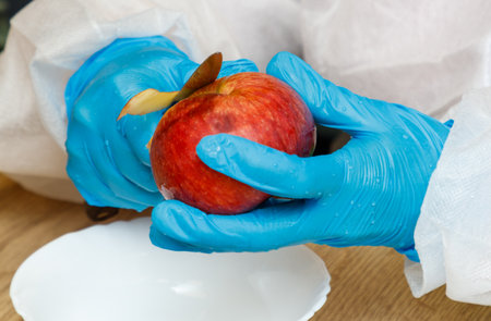 A person is cutting an apple with a knife. The apple is in a bowl. The person is wearing blue gloves.の写真素材