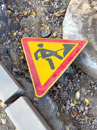 A triangular sign depicting a man holding a shovel. The sign is located on the ground.