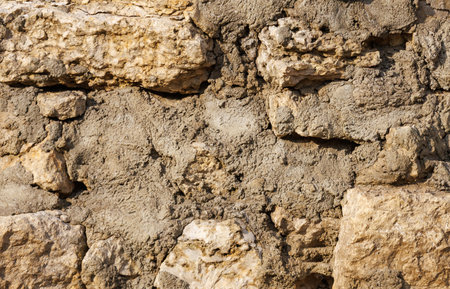 A wall made of rocks and dirt. The wall is brown and has a rough texture. There are some holes in the wallの写真素材