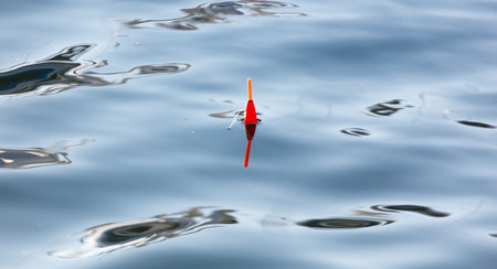A red fishing lure is floating on the surface of the water. The water is calm and clearの写真素材
