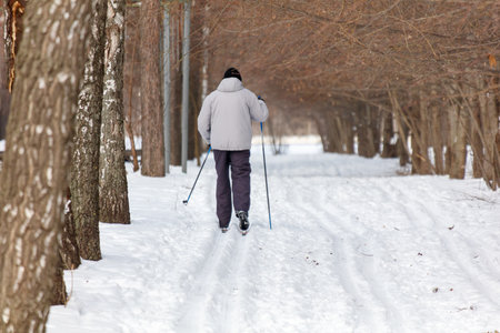 A man is skiing on a snow-covered path. He is wearing a gray jacket and blue pantsの写真素材