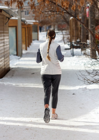A woman is running in the snow. She is wearing a white jacket and black pants. The snow is white and the ground is covered in snowの写真素材