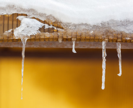 Icicles hanging from a roof. The roof is yellowの写真素材