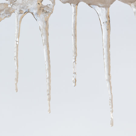 A long, thin icicle hangs from the roof, dripping with water. The icicle is almost as long as the roof itself, and it is clear that it has been there for some timeの写真素材