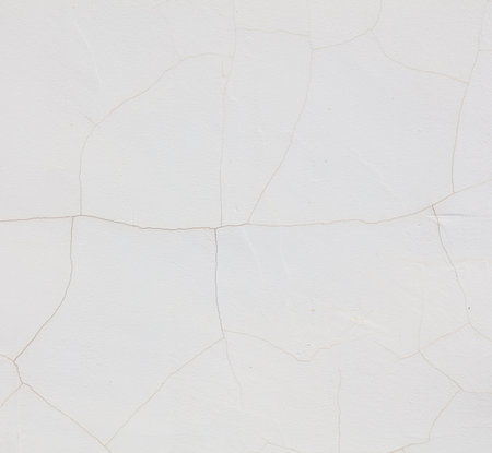 A white wall with cracks and holes. The wall is white and has a lot of cracks. The cracks are in different sizes and shapesの写真素材
