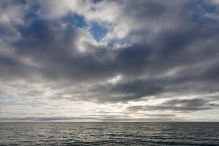 A cloudy sky with a large body of water in the background. The sky is mostly cloudy with a few patches of blue skyの写真素材