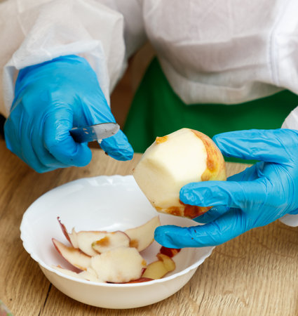 A person is cutting an apple with a knife. The apple is in a bowl. The person is wearing blue glovesの写真素材