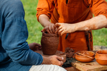 Man is making a pottery vase. Another man is helping him. There are several bowls and a cup on the...