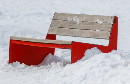 A red bench is sitting in the snow. The bench is emptyの写真素材